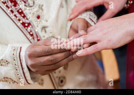 Indischer Bräutigam, der während der Hochzeit einen Ring auf eine Hand der Bräute legt Zeremonie Stockfoto