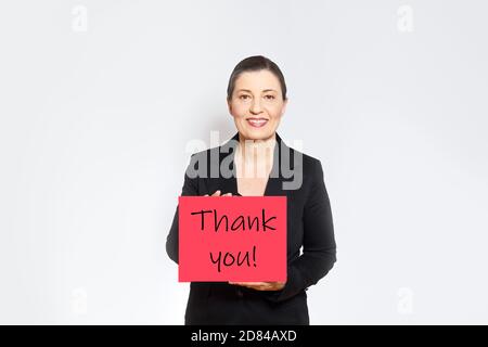 Lächelnder Arbeitgeber in schwarzem Business-Outfit hält eine rote Karte mit Text Danke! Stockfoto