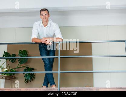 Junger Mann, der auf der Terrasse in seiner Wohnung steht. Stockfoto