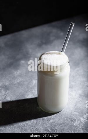 Ayran türkischer Schaumjoghurt-Drink im Glas mit Stroh auf grauem Hintergrund. Gesundes probiotisches Getränk Stockfoto