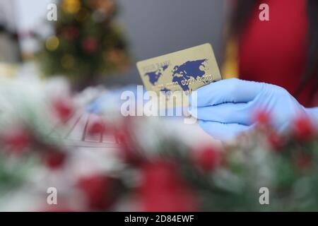 Hand in Handschuh hält eine Plastikkarte vor dem Hintergrund Der Neujahrsdekoration Stockfoto