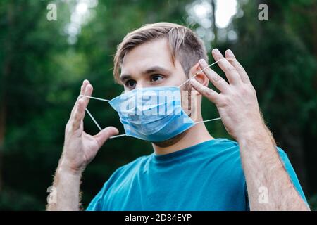 Mann Porträt trägt blaue medizinische Maske im Gesicht. Kaukasischer Mann trägt chirurgische Einweg-medizinische Maske gegen Coronavirus, Epidemie covid 19, Smog Stockfoto