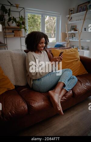 Schöne afrikanische Frau, die Video auf dem Smartphone zu Hause, während Entspannen auf der Couch Stockfoto