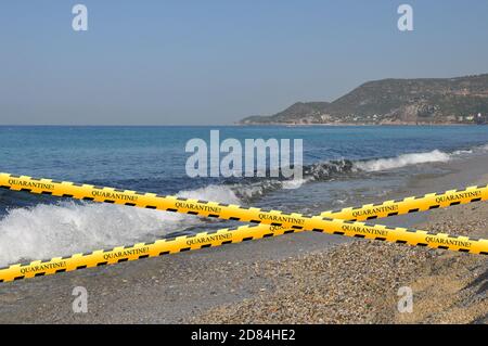 Sperrband. Quarantäne-Inschrift auf schwarzem, gelbem Band. Leerer Strand Stockfoto