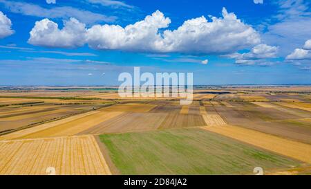 Blick über landwirtschaftliche Felder, kultivierte Parzellen in der Erntezeit, blauer Himmel mit weißen flauschigen Wolken ihre Schatten sind auf dem Boden. Stockfoto