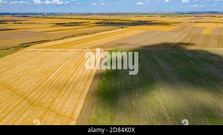 Blick über landwirtschaftliche Felder, kultivierte Parzellen in der Erntezeit, blauer Himmel mit weißen flauschigen Wolken ihre Schatten sind auf dem Boden. Stockfoto