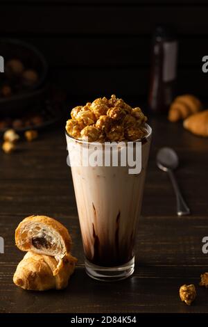 Hohe Glas Tasse mit Schokolade Milchshake und Karamell Popcorn und Schokoladenmuffin auf Holzhintergrund Stockfoto