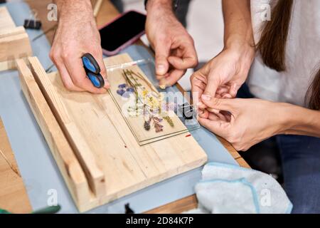 Eine Frau fixiert Glasplatten. Meisterkurs zur Rahmenerstellung mit Herbarium in tiffany-Technik in Buntglas. Herbarium von getrockneten verschiedenen Pflanzen Stockfoto