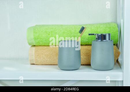 Hellgraue Keramik Accessoires für Bad - Seifenspender, Holzzahnbürste und Handtücher für die persönliche Hygiene. Einrichtung im Badezimmer. Stockfoto