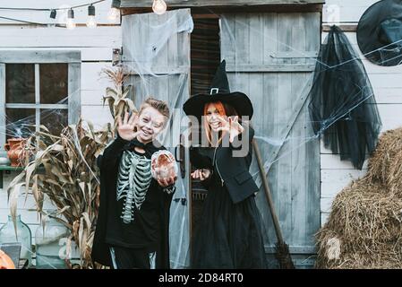 Kinder ein Junge in einem Skelett Kostüm und ein Mädchen In einem Hexenkostüm mit Spaß auf einer Halloween-Party Auf der dekorierten Veranda Stockfoto