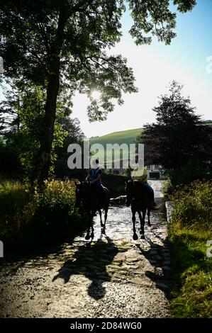 Die berühmte Malmsmead-Brücke, umgeben von grünen Bäumen, an denen eine furt entlang läuft, Pferde, die durch das Wasser laufen, Lorna Doone Country, Exmoor Stockfoto