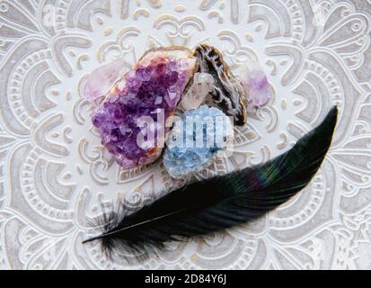 Flache Ansicht von verschiedenen Kristallgeoden Amethyst, Celestit. Mit schwarz glühender Vogelfeder. Stockfoto