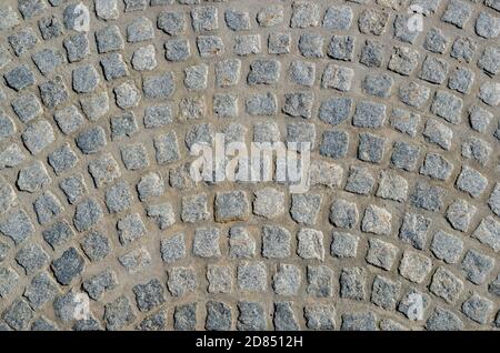 Ein Fragment von Bürgersteig gepflastert mit rauen quadratischen grauen Steinblöcken mit unebenen Kanten in Form von halbrunden gewölbten Streifen. Stockfoto