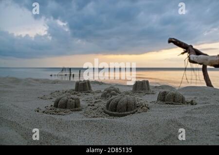 Kinderfiguren aus grauem Sand mit Kuppelgras und Beulen Auf dem Hintergrund des Meeres und des blauen Himmels spiegelte sich dort mit Dunkle Wolken vor dem Sturm Stockfoto