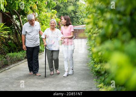 Glückliche Familie, die gemeinsam im Garten spazieren geht. Alte ältere Menschen mit einem Gehstock zu helfen, Gleichgewicht zu gehen. Konzept der Liebe und Pflege der Familie und Gesundheit Stockfoto