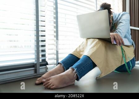 Gestresste asiatische Unternehmerin sitzt neben dem Fenster, weil ihr Geschäft aufgehört hat, Geschäfte zu machen. Aufgrund finanzieller Probleme und der Konjunkturabschwächung Stockfoto