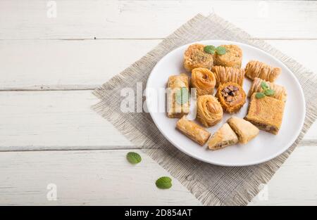 Traditionelle arabische Süßigkeiten (Kunafa, Baklava) auf weißem Holzhintergrund und Leinentextilien. Seitenansicht, Kopierraum. Stockfoto