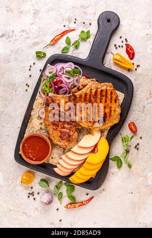 Gegrilltes Schweinebrippensteak auf einem Tonteller mit Öl, Senf, Salz und Rosmarin auf einem alten rustikalen Holztisch. Draufsicht, flach liegend. Stockfoto