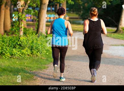 Rückansicht von zwei Frauen auf einem Lauf in einem Park auf einem unbefestigten Pfad rund um Belmont Lake. Stockfoto