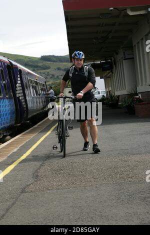 Girvan Railway Station, South Ayrshire, Schottland, Großbritannien. Ein Radfahrer mit Shorts und Schutzhelm kommt mit dem Zug am Bahnhof Girvan an, bevor er eine Radtour startet Stockfoto