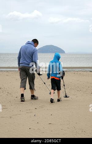 Girvan, Ayrshire, Schottland, Großbritannien. Eine Familie am Strand Metall entdeckt auf der Suche nach Schatz, im Hintergrund kann der ikonische Ailsa Craig gesehen werden Stockfoto