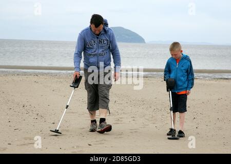 Girvan, Ayrshire, Schottland, Großbritannien. Eine Familie am Strand Metall entdeckt auf der Suche nach Schatz, im Hintergrund kann der ikonische Ailsa Craig gesehen werden Stockfoto