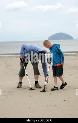 Girvan, Ayrshire, Schottland, Großbritannien. Eine Familie am Strand Metall entdeckt auf der Suche nach Schatz, im Hintergrund kann der ikonische Ailsa Craig gesehen werden Stockfoto