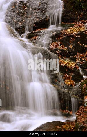 Kaskadierende Wasser spritzt über Granitfelsen mit bunten Herbstblättern Stockfoto