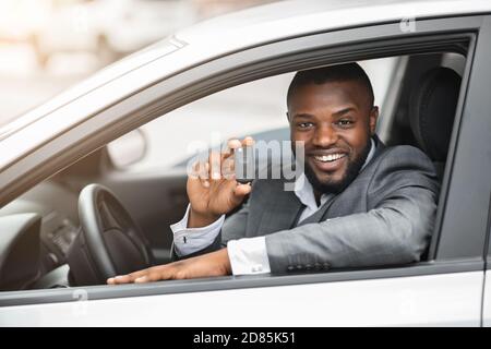 Glücklich schwarz Kerl in Anzug hält Schlüssel aus neuen Auto Stockfoto