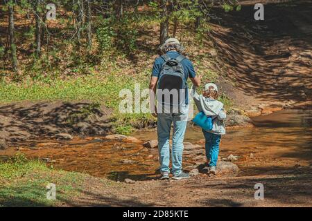 Vater und Sohn überqueren den Bach im Wald. Mann und Kind mit Rucksäcken auf dem Hintergrund des Waldes. Reisekonzept mit Kindern. Lifestyle. Stockfoto