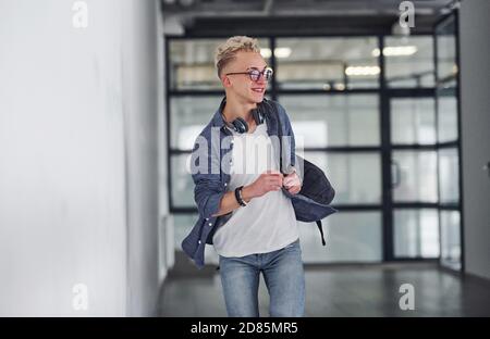 Junge Student in legerer Kleidung geht drinnen mit Rucksack Stockfoto