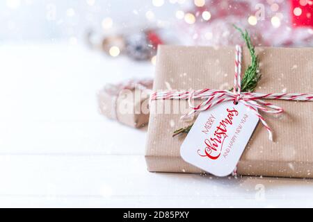 Frohe Weihnachten und glückliches neues Jahr Öko-Geschenk mit Tag und Fichtenzweig. Glühender Schnee Bokeh. Winterurlaub auf weißem Hintergrund. Kein Abfall, Kunststoff f Stockfoto