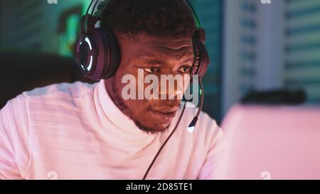 Glücklicher junger schwarzer Mann mit beleuchtetem Headset mit Laptop. Home Office- und Remote-Work-Konzept. Porträt des Aktienhändlers. Hochwertige Fotos Stockfoto