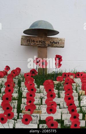 Moffat, Dumfrieshire, Schottland, Großbritannien, Gedenkstätte für den 1. Weltkrieg vor einem Dorfladen, 100yrs seit Ende WW1. Mohnreihen auf Holzkreuzen mit einem WW1-Helm auf einem größeren Kreuz Stockfoto