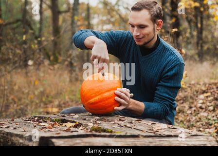 Ein junger Mann stitzt draußen das Gesicht eines Kürbisses, Stockfoto