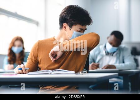 Asiatisch männlich Student Couching in seinem Ellbogen, Niesen in Ärmel Stockfoto