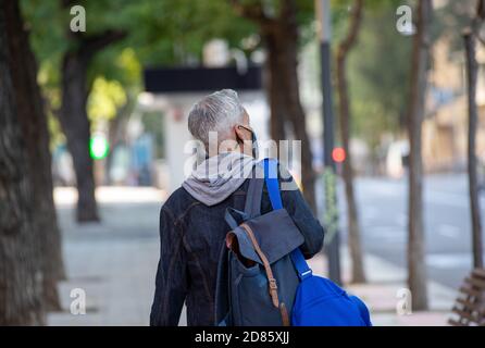 Rückansicht des anonymen männlichen Touristen in Maske und mit Rucksack zu Fuß entlang der Straße in Madrid und genießen Sie die Aussicht auf Stadt Stockfoto