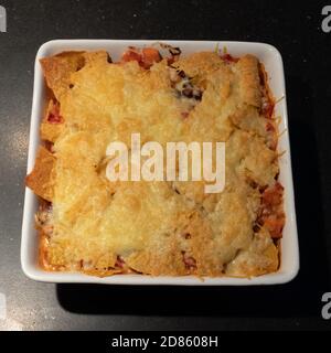 Lasagne serviert auf einem weißen Teller in einer dunklen Küche Tischplatte Stockfoto