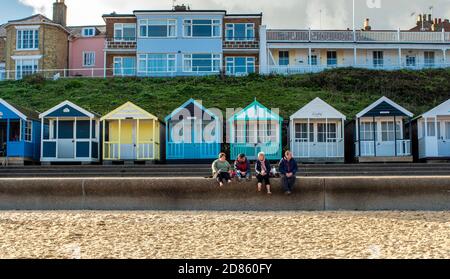 Vier Leute sitzen auf der Promenade mit Strandhütten dahinter, Southwold, Suffolk, Großbritannien Stockfoto