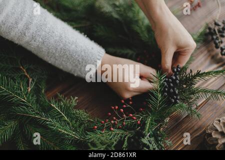 Herstellung rustikalen weihnachtskranz, saisonalen Winter-Workshop. Floristen Hände halten Beeren und machen weihnachtskranz auf Holztisch mit natürlichen Festi Stockfoto