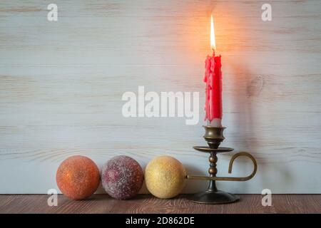 Weihnachtsdekoration. Brennende rote Kerze auf Kerzenständer und Kugeln auf weißem Holzhintergrund mit Platz für Text. Stockfoto