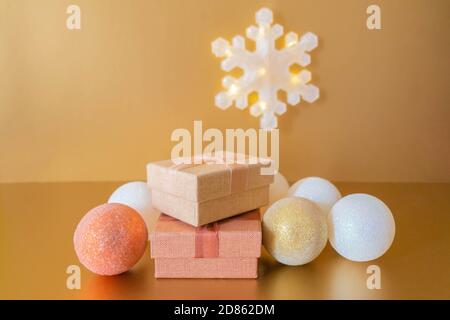 Goldene Weihnachtsdekoration mit Geschenkschachteln, Kugeln und glänzender Schneeflocke. Weihnachtsstimmung. Komposition mit Weihnachtskugeln Geschenkschachteln auf goldenem Tisch Stockfoto