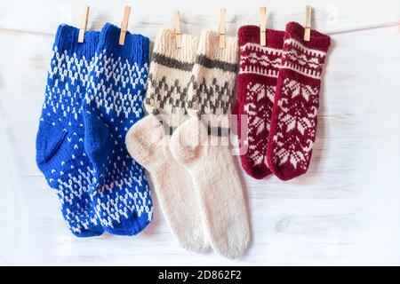 Gestrickte Wollsocken und Fäustlinge hängen auf Wäscheklammern auf Holzhintergrund. Frankreich Flagge Farben Vintage Dekoration. Winter- und Weihnachtskonzept Stockfoto