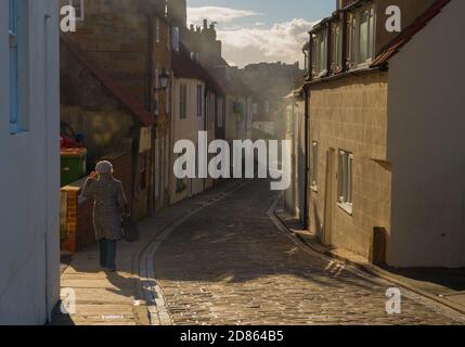 Frau, die in der Altstadt von Whitby, North Yorkshire, eine Seitenstraße entlang läuft. Stockfoto