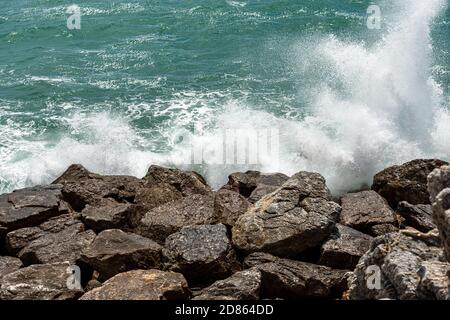 Weiße Wellen des Meeres stürzen auf die Felsen. Wellenbrecher aus großen Felsbrocken im Golf von La Spezia, Ligurien, Italien Stockfoto