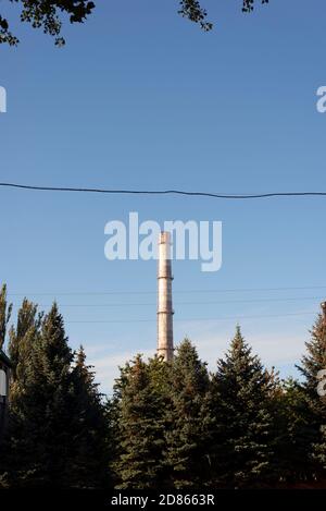 Rauchfreier Pflanzenkamin in Baumrahmen hohen industriellen Schornsteinstapeln Hell erleuchtet gegen fast schwarzen dramatischen Himmel Stockfoto