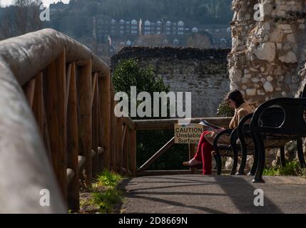 Guildford, Vereinigtes Königreich - 05. Mai 2019 : EINE junge Frau sitzt Buch auf Holzbank in Guildford Castle und Gelände. Kein Fokus, speziell. Stockfoto