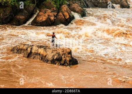 Champasak, Laos - 24. OKTOBER 2010: Laotischer Fischer steht auf der Schnellmaschine und wirft Fischernetz auf den Mekong. Li Phi Wasserfall. Stockfoto