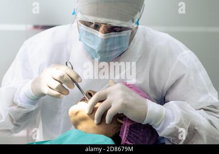 Der Zahnarzt oder Arzt trägt im Hintergrund der Zahnarztpraxis einen weißen medizinischen Kittel, eine Maske und eine Schutzbrille. Gesundheits- und Schutzkonzept Stockfoto