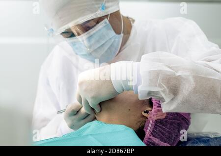 Der Zahnarzt oder Arzt trägt im Hintergrund der Zahnarztpraxis einen weißen medizinischen Kittel, eine Maske und eine Schutzbrille. Gesundheits- und Schutzkonzept Stockfoto